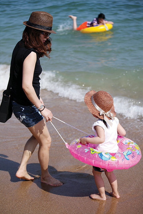 바닷가에 튜브를 끼고 선 아이와 튜브줄을 잡고 있는 엄마