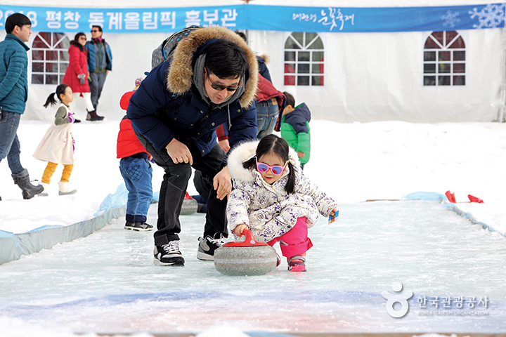 평창 동계올림픽 홍보관 앞에서 컬링공을 밀어보는 어린아이, 뒤에서 아빠가 보고있다