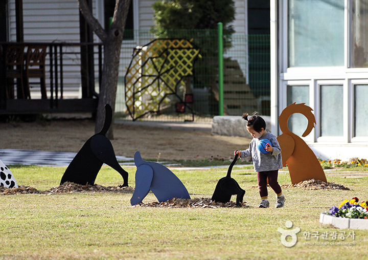 잔디밭에 전시되어 있는 땅파는 강아지 모형을 신기하게 바라보는 꼬마 아이
