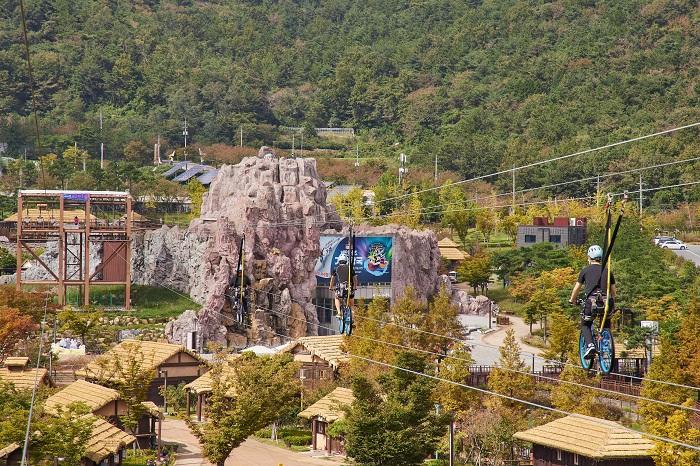 The exiting cycles run in the air in Gimhae Gaya Theme Park.Beyond the cycles, there are a rocky-mountain-shaped Cheolgwangsan Performance Hall and Gaya Folk Village with thatched houses.
