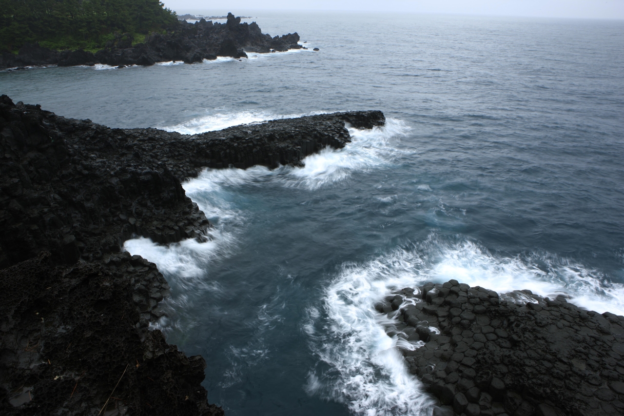 Black basalt columnar cliffs with white surf along the Jungmun coast of Jeju