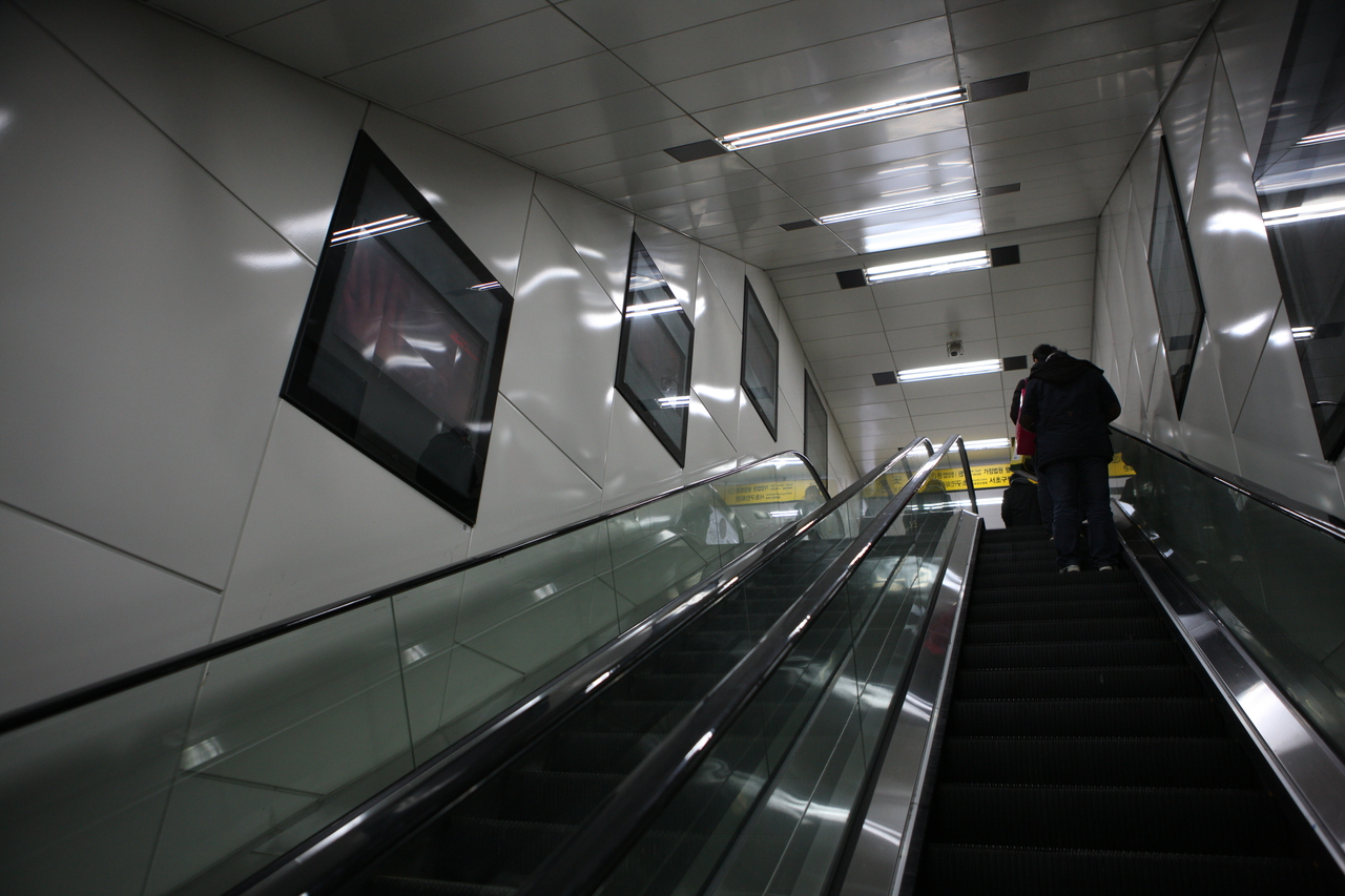 An escalator rising towards the exit of Yangjae subway station in Seoul, with yellow Korean exit signage at the top — ⓒ한국관광공사 포토코리아-김지호 (Korea Tourism Organization, KOGL Type 1)