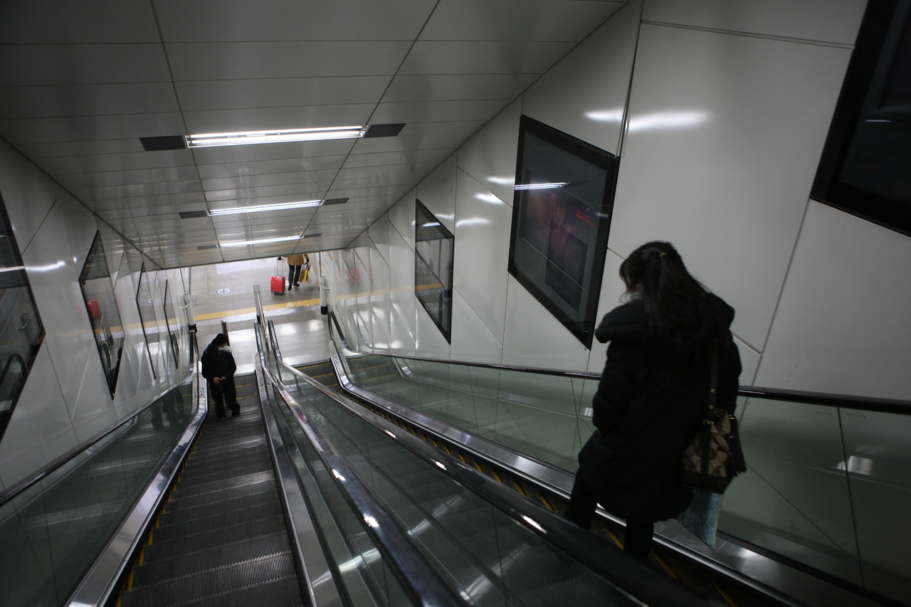 A clean, brightly lit subway station escalator leading down to a platform