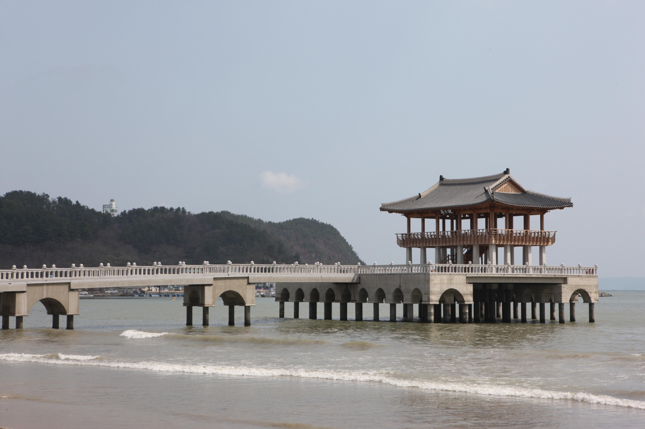 A tiled-roof pavilion standing on pillars over the sea, reached by a causeway from the beach at Yeongildae